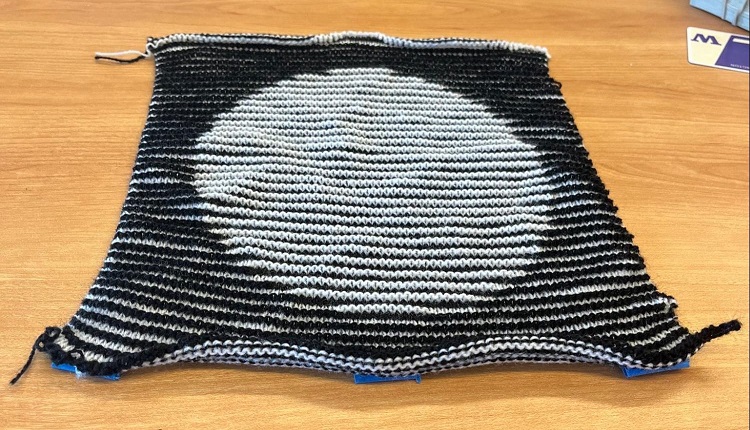 The same knitted piece when viewed at an angle. Now the circle is plainly visible as a filled-in white shape with a black background.