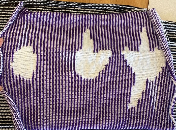 A knit object from a head-on view depicting three white shapes on a purple-and-white striped background, placed side-by-side. The first shape is a circle. The second shape is the top and right leg of a star. The last shape is the top, left, right, and bottom left legs of a star.