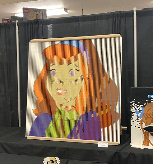 A picture of a large flat sheet made of Lego. Two portraits of Daphne from Scooby Doo and Azula from Avatar: The Last Airbender are interleaved such that 2nth row is coloured to look like the nth row of Daphne's picture, and the 2n+1th row is coloured to look like the nth row of Azula's picture.