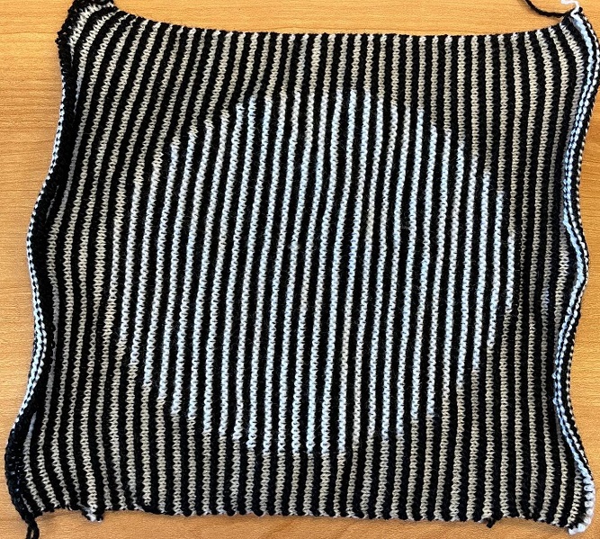 A top-down view of the above image turned into an illusion knit. The knit object is made of alternating black and white stripes. Even in the head-on view, you can see the outline of the circle, because the raised white stitches inside the circle are hitting the light, and the flat white stitches outside the circle are in shadow.